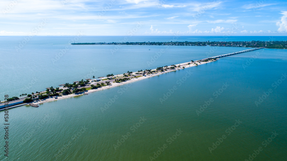 Obraz premium Aerial Drone of the Causeway Bridge Before Hurricane Ian in Sanibel, Florida with the Bay and a Preserve in the Foreground and the Gulf of Mexico in the Background Featuring a Blue Sky and Blue Water