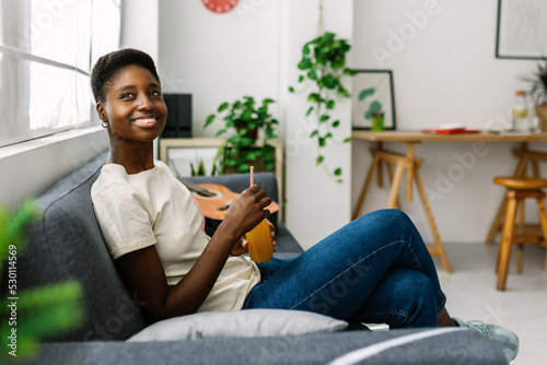 Bilde på lerret Young african woman chilling on sofa drinking orange juice - Millennial dreamy f