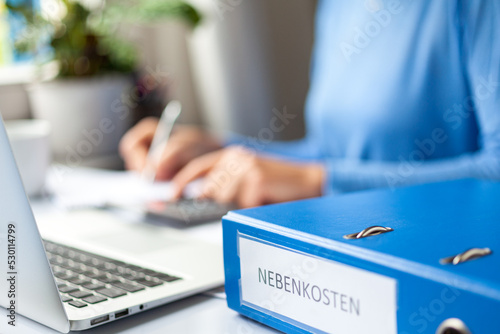 Symbolfoto hohe Nebenkosten für Mieter - Frau sitzt zu Hause am Schreibtisch und überprüft die erhöhte Aufstellung der monatlichen Abschläge für Strom und Gas photo