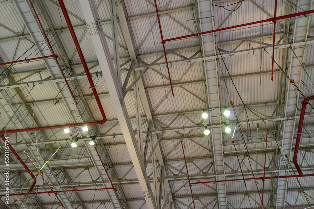 The steel construction roof of a sports hall and the spot lights on this roof. Wide shot of industrial hall empty and clean. Empty factory interior or storehouse
