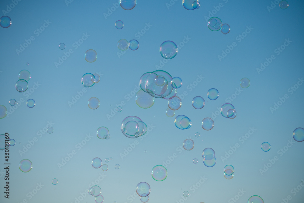 Big bubble flying over blue sky. Huge colorful soap bubbles fly over cloudy sky background.