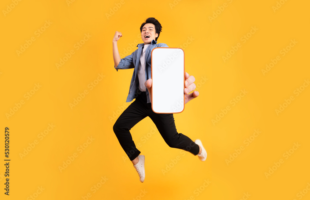 image of jumping up asian man holding smartphone in hand, isolated on yellow background image of jumping up asian man holding smartphone in hand, isolated on yellow background
