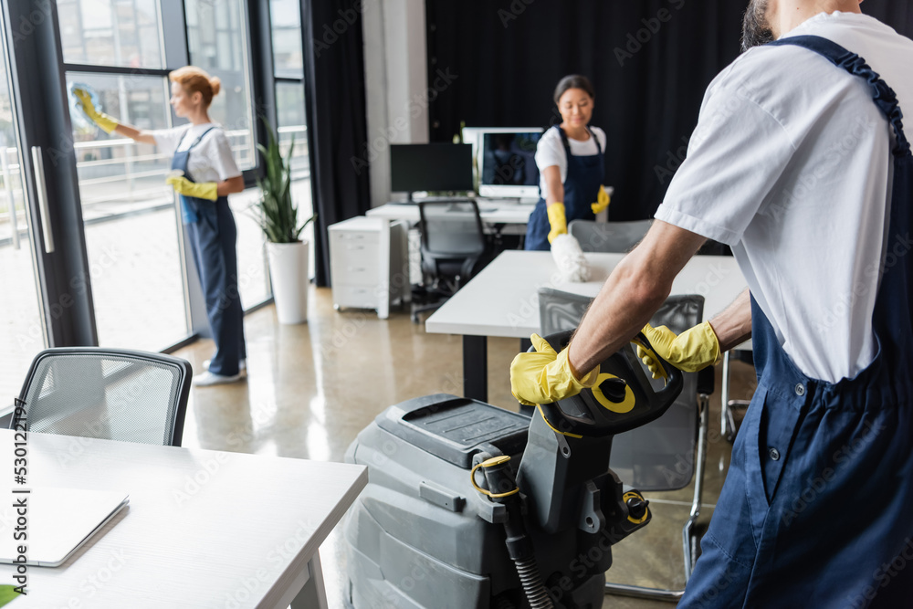 man with floor scrubber machine near multiethnic women washing windows and furniture. man with floor scrubber machine near multiethnic women washing windows and furniture.