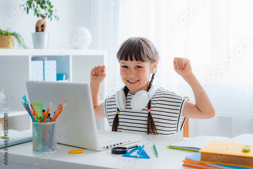 Child brunette schoolgirl studying homework during an online lesson at home in a bright white room, school time, online education concept