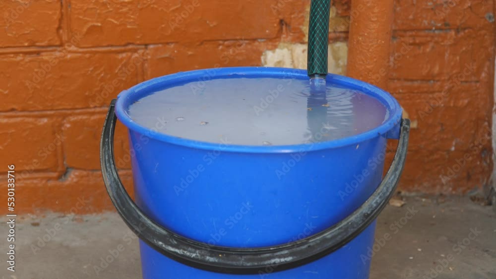 The water from the hose has filled the bucket and is overflowing The water from the hose has filled the bucket and is overflowing