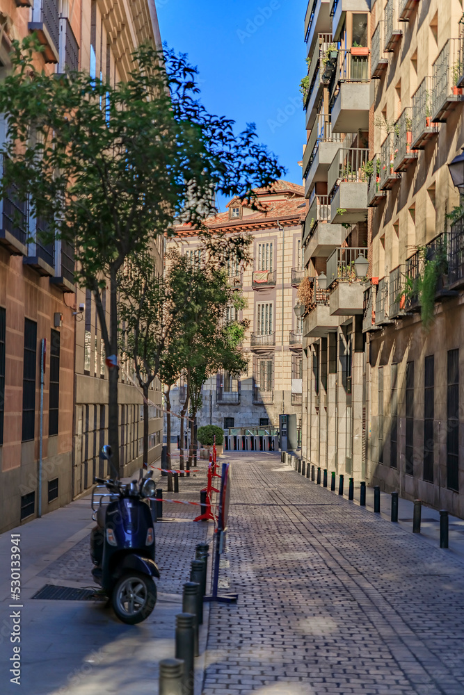 Beautiful traditional residential buildings with metal balconies on a narrow cobblestone street of the city center in Madrid, Spain