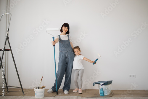 Young mother and a funny child girl have fun during the repair holding paint rollers on hands. Renovation of the rooms of the house, a new house and moving.