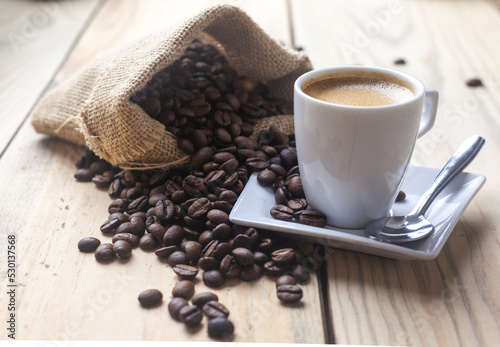 Taza de café sobre un platillo junto a un saco con granos de cafe