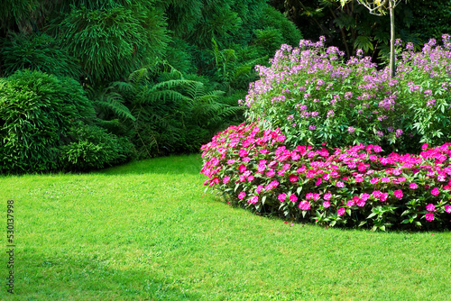 Circular flowerbed with flowers and green lawn, green trees and hedges