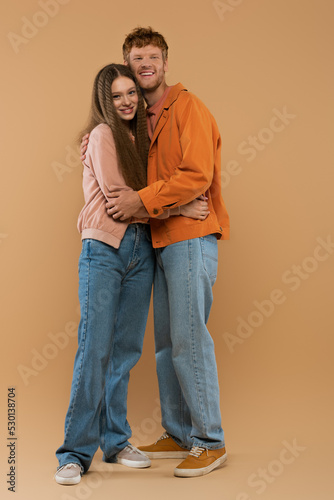 full length of young and cheerful couple hugging while standing on beige. © LIGHTFIELD STUDIOS