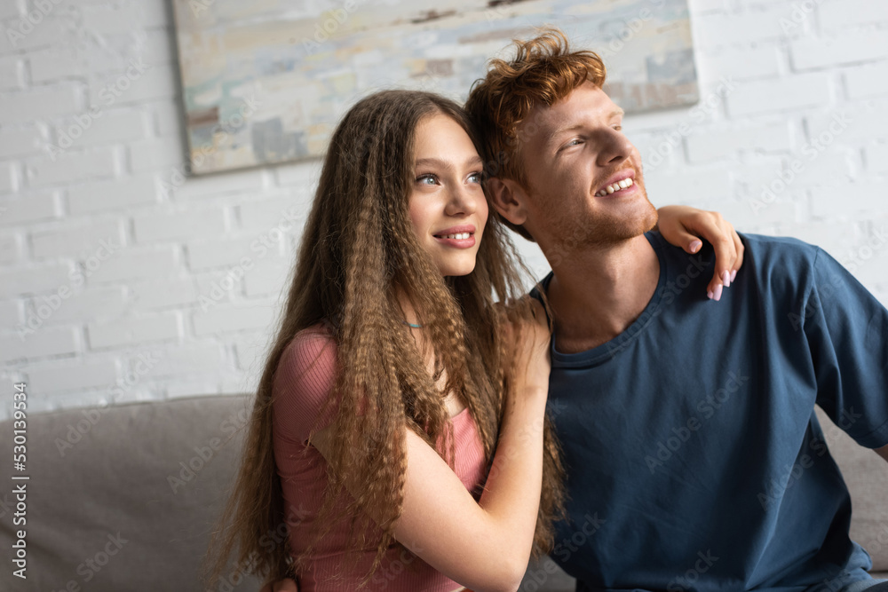 cheerful and young man and cheerful girlfriend smiling while looking away. cheerful and young man and cheerful girlfriend smiling while looking away.