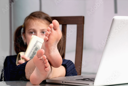 Humorous portrait of happy cute young business girl counts money profit with bare feet on the table. Selective focus on bare feet. Copy space for text or design. photo