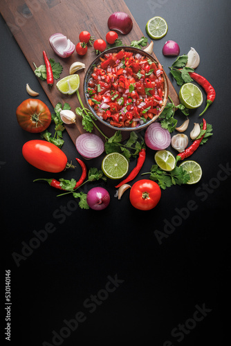 Flat lay view of resh salsa made with homegrown ingredients of tomatoes, red onions, garlic, chili peppers, cilantro and lime on a black background with space for text