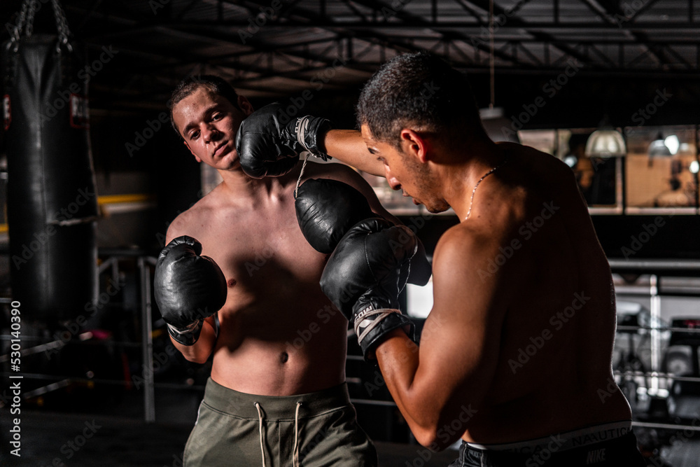 High quality photography. Two men boxing in a gym. A Caucasian man and a Latino man boxing in a boxing ring inside a gym. Two people sparring.
