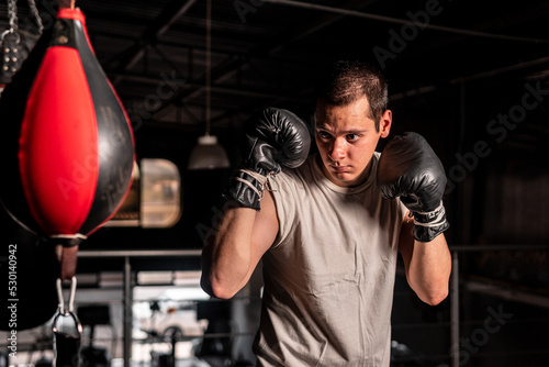 High quality photography. Boxer in defense position about to deliver a blow to a punching bag. Short-haired Caucasian man wearing boxing gloves in a gym. © Wacha Studio