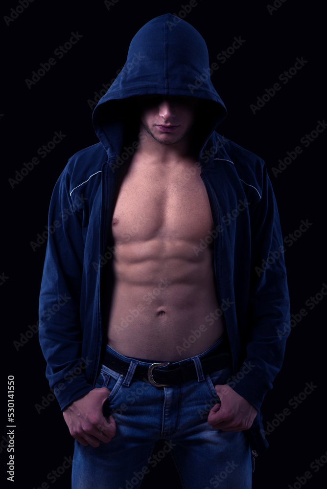 Young muscular man wearing hoodie sweater and jeans standing against black background