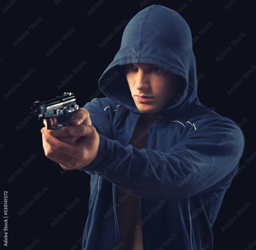 Young man criminal shooting with gun isolated on black background Young man criminal shooting with gun isolated on black background