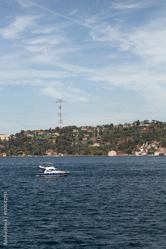 View of a yacht passing on Bosphorus and Asian side of Istanbul. It is a sunny summer day.Beautiful travel scene. View of a yacht passing on Bosphorus and Asian side of Istanbul. It is a sunny summer day.Beautiful travel scene.
