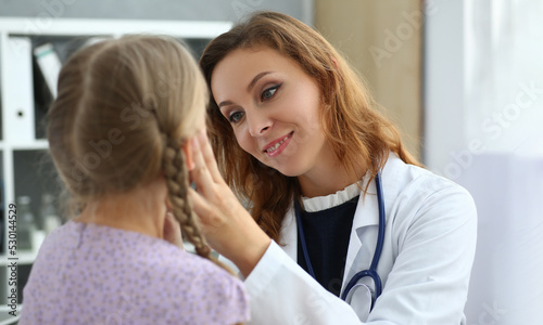 Female doctor checks throat of little girl in medical office