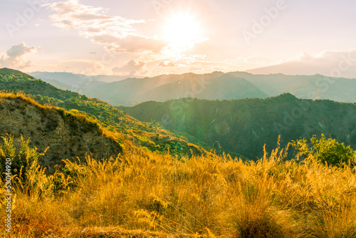 beautiful highland landscape with amazing view from a top with golden grass and green bushes to a canyon with majectic mountains and scenic cloudy sunset on background