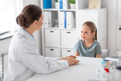 medicine, healthcare and pediatry concept - female doctor or pediatrician talking to little girl patient on medical exam at clinic