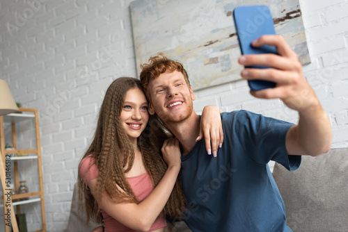 young and happy man taking selfie with positive girlfriend in living room.