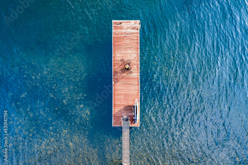 Wooden dock on a lake overhead aerial with clear blue water.