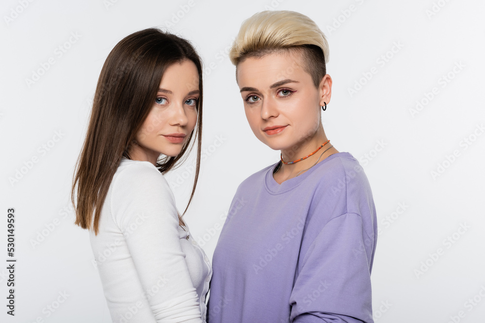 brunette and blonde lesbian couple with makeup looking at camera isolated on grey. brunette and blonde lesbian couple with makeup looking at camera isolated on grey.