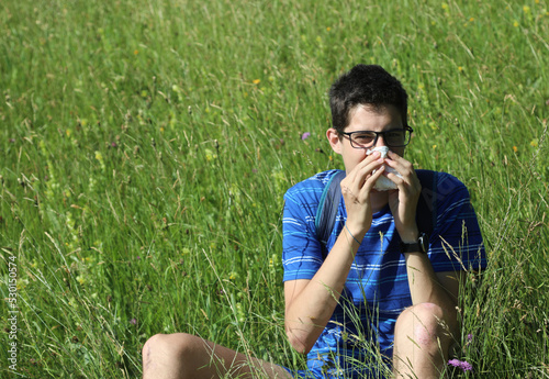 young boy with glasses blowing his nose because of allergy in the meadow photo