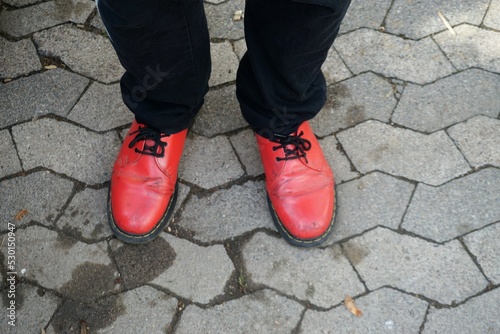 Mann in rotem Lederschuhen und schwarzen Hosenbeinen auf grauem Pflastersteinplatz in Stadt  © Anette
