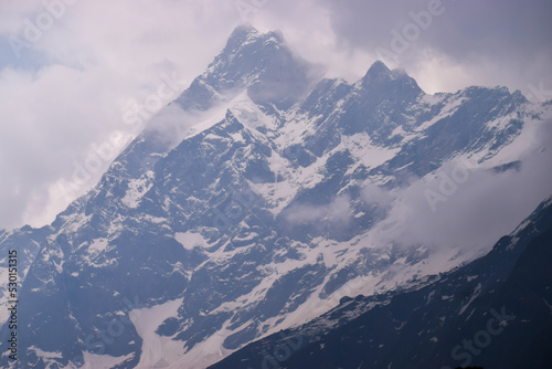Snow covered peak of Mount Swargarohini in the Himalayas in Uttarakhand, India. Close view of cloud covered swargarohini peak and glaciers at an elevation of 6252 meters seen from har ki dun valley.