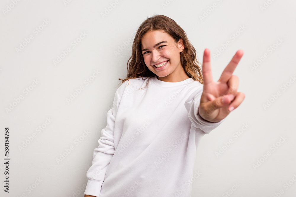 Young caucasian woman isolated on blue background joyful and carefree showing a peace symbol with fingers. Young caucasian woman isolated on blue background joyful and carefree showing a peace symbol with fingers.
