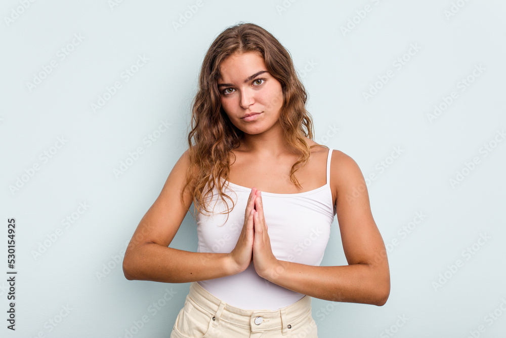 Young caucasian woman isolated on blue background praying, showing devotion, religious person looking for divine inspiration. Young caucasian woman isolated on blue background praying, showing devotion, religious person looking for divine inspiration.
