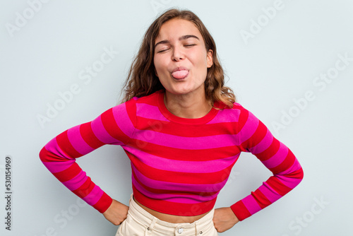 Foto Young caucasian woman isolated on blue background funny and friendly sticking out tongue