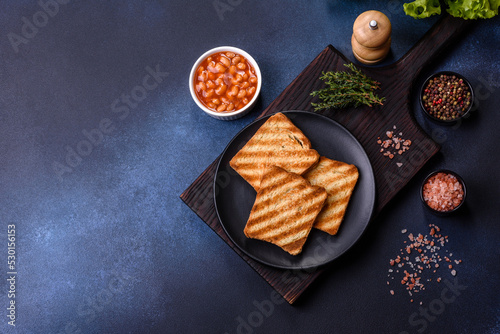 Traditional English breakfast with eggs, toast, sausages, beans, spices and herbs on a grey ceramic plate