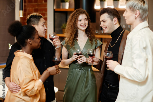 Group of young multicultural friends in casualwear toasting at home party and chatting while standing in front of each other in the kitchen
