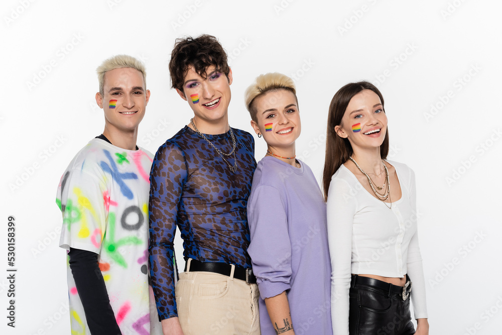 Obraz premium smiling lgbtq community friends with rainbow flags on faces looking at camera isolated on grey.