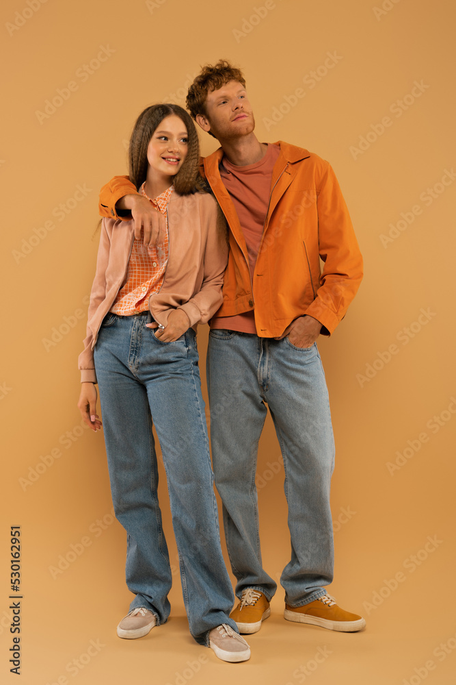 full length of happy young man in autumnal outfit and gumshoes hugging girlfriend on beige. full length of happy young man in autumnal outfit and gumshoes hugging girlfriend on beige.