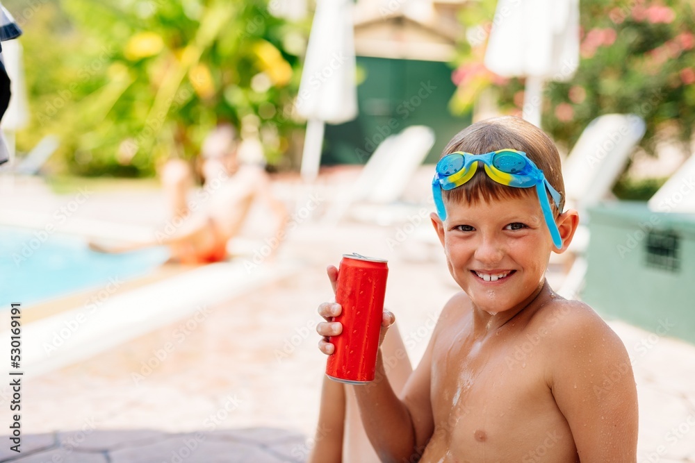 Happy boy is drinking a carbonated drink from a red can in the pool. Happy holidays Corfu, Greece