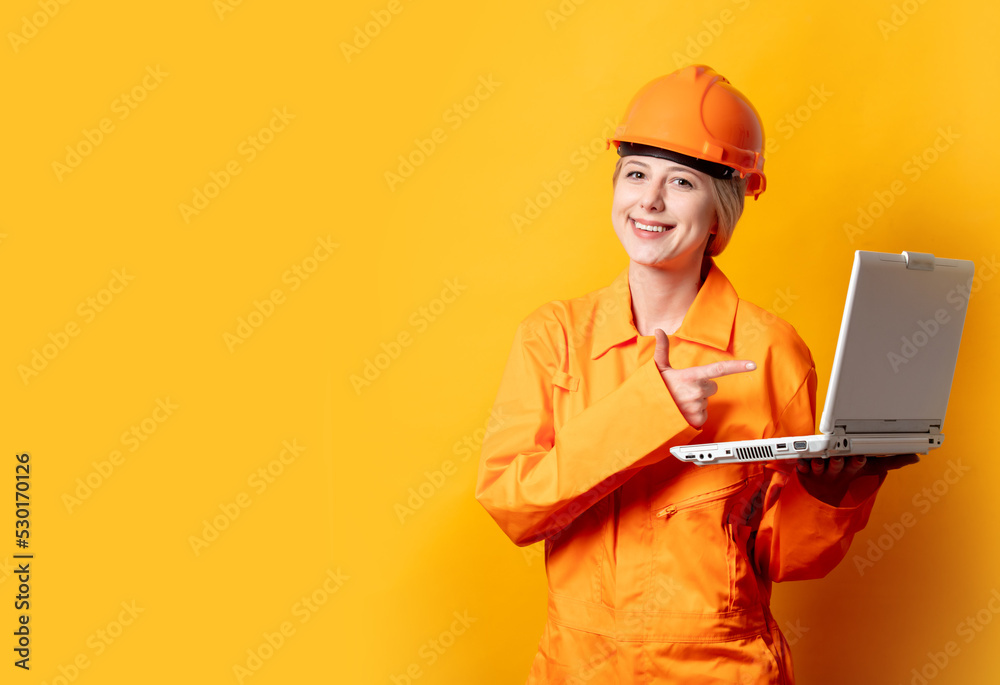woman construction worker in helmet and orange overalls holding a laptop woman construction worker in helmet and orange overalls holding a laptop
