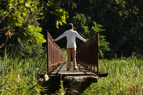 Young man in a white shirt standing on a narrow bridge. Pavel, i on narrow bridge and summer nature around me. Photo was taken 24 August 2022 year, MSK time in Russia.