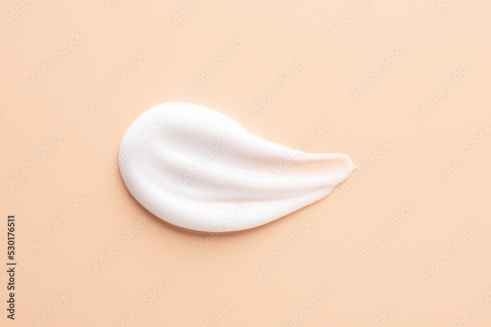 Texture of cosmetic product for face care. White smear of cosmetic cream on beige background. Top view closeup