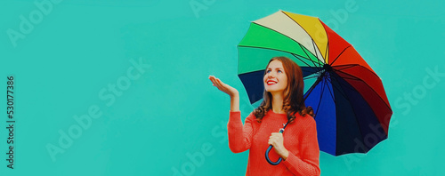 Autumn portrait of happy smiling young woman holding colorful umbrella wearing red knitted sweater on blue background