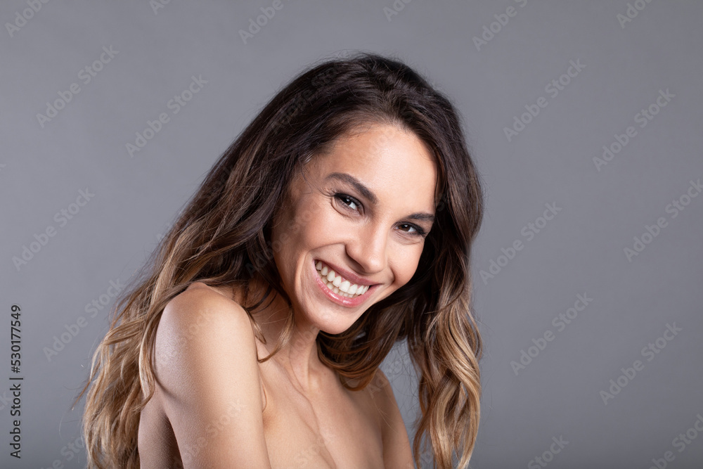 Close-up attractive girl smiling sweetly on gray isolated background. Woman with long wavy hair and wide smile. Close-up attractive girl smiling sweetly on gray isolated background. Woman with long wavy hair and wide smile.