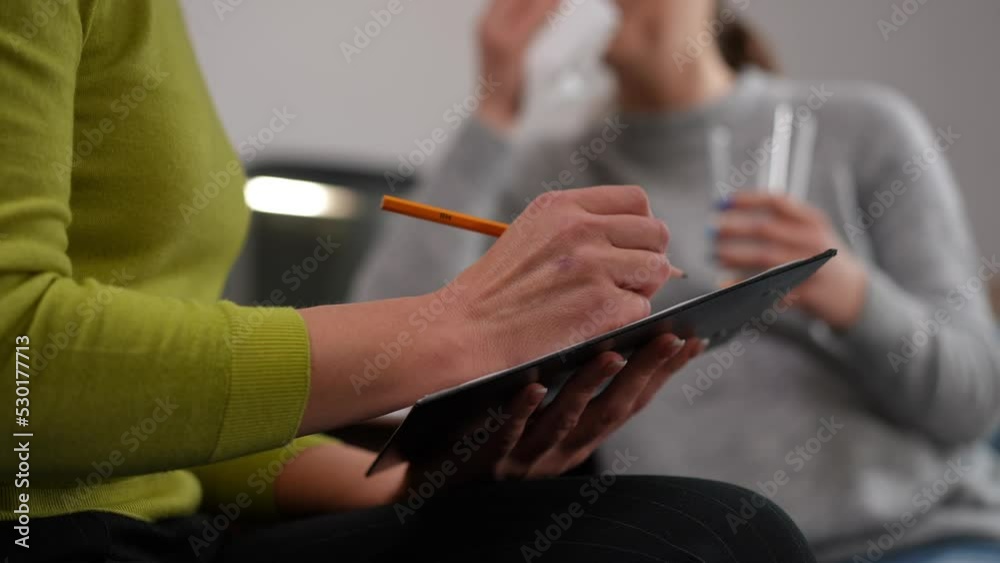 Close-up unrecognizable psychotherapist writing with blurred pregnant woman crying at background sitting with glass of water. Caucasian professional doctor consulting depressed expectant indoors Close-up unrecognizable psychotherapist writing with blurred pregnant woman crying at background sitting with glass of water. Caucasian professional doctor consulting depressed expectant indoors