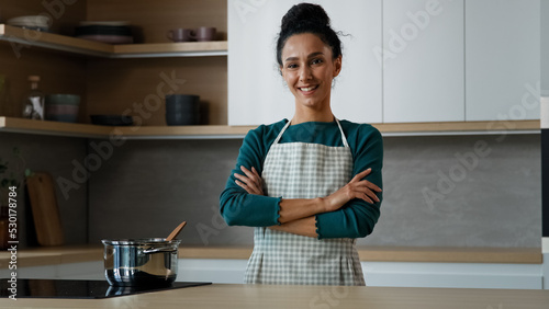 Fotografija Cheerful beautiful woman wears apron standing in modern kitchen with crossed han