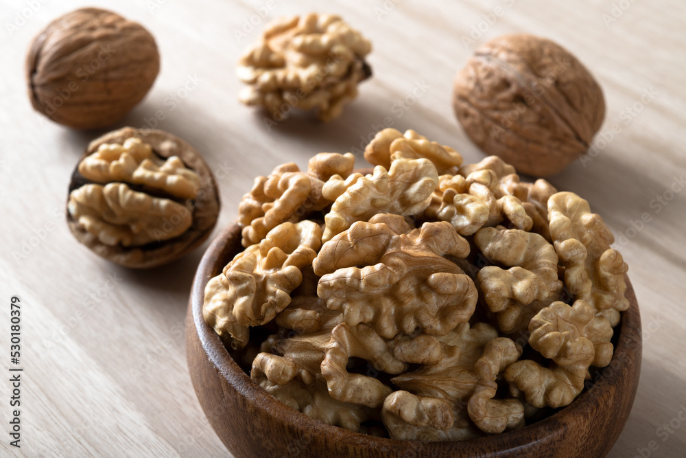 Peeled walnuts and whole walnuts in wooden bowl
