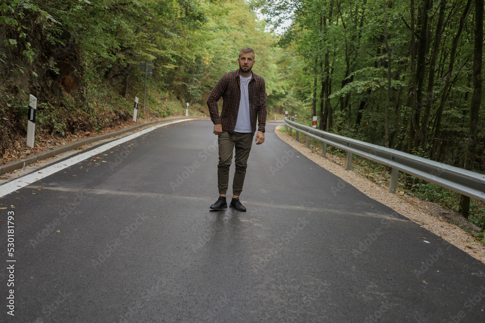 a young man is walking near the road and in the forest a young man is walking near the road and in the forest
