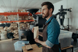 Business owner holding roasted coffee beans in paper bag in coffee factory and looking at side