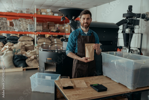 Business owner holding roasted coffee beans in paper bag in coffee factory